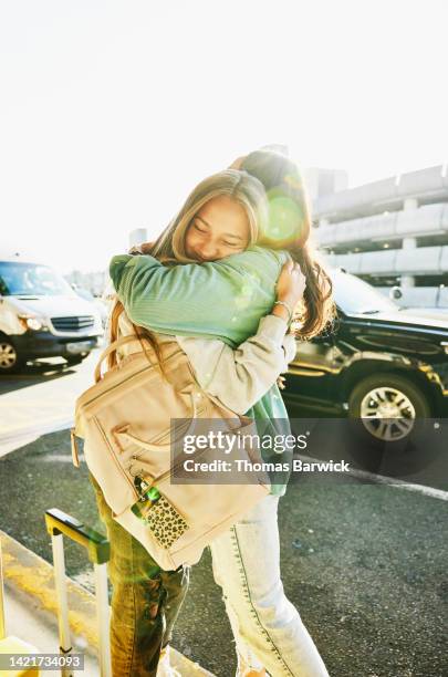 medium wide shot of mother and daughter hugging curbside at airport - family hugging bright stock pictures, royalty-free photos & images