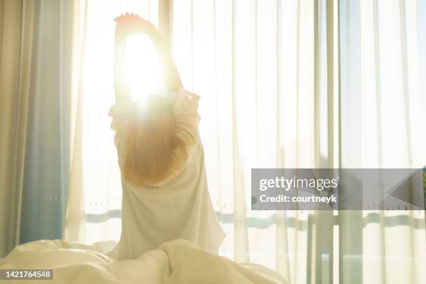 woman wearing nightwear waking and stretching in the morning light. - awake day stockfoto's en -beelden