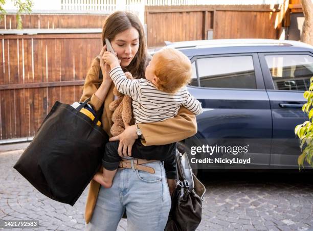 loving woman carrying her son talking on cell phone in driveway - baby bag stockfoto's en -beelden