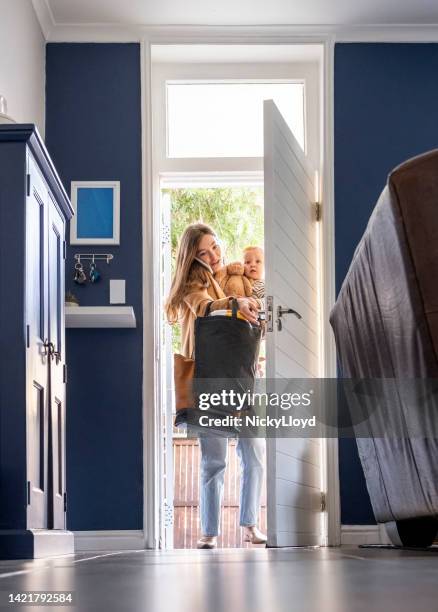 mother carrying son talking on phone and entering the house from front door - terugkomen stockfoto's en -beelden