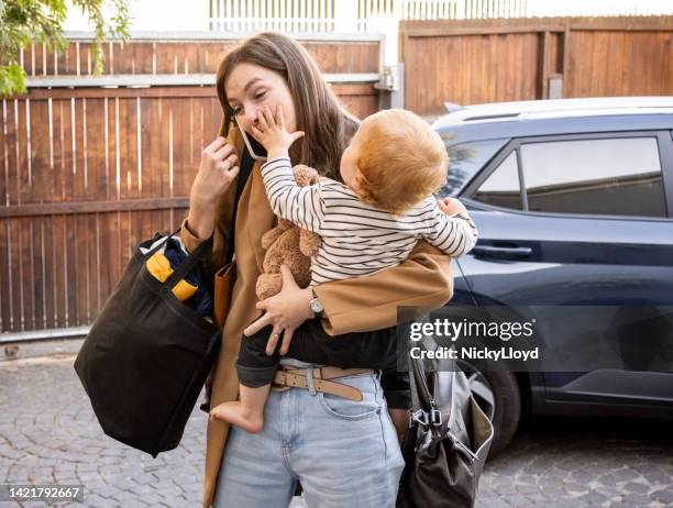 woman carrying her son talking on mobile phone in driveway - baby bag stockfoto's en -beelden