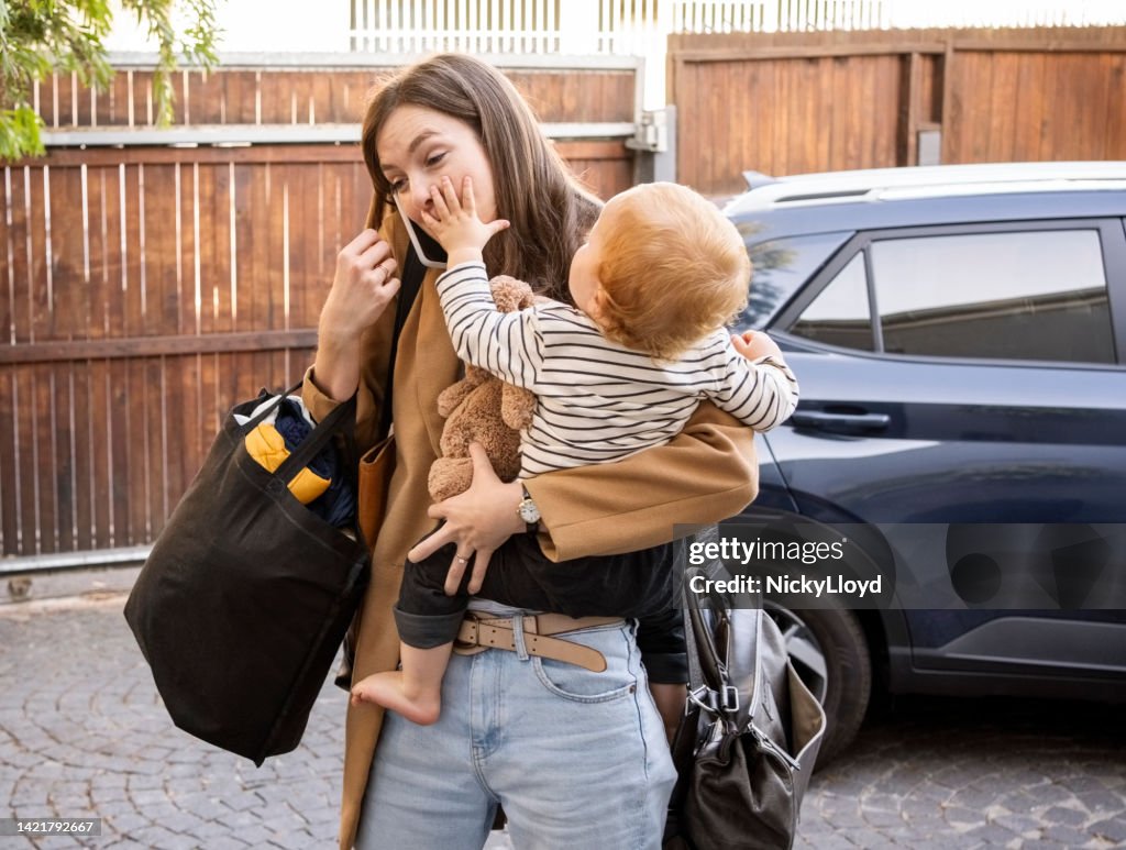 Woman carrying her son talking on mobile phone in driveway