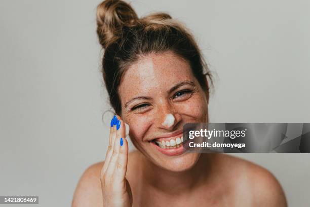 happy freckled woman applying moisturizing cream on face - beauty studio moisturisers stock pictures, royalty-free photos & images