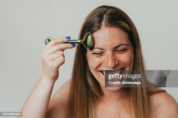 smiling freckled woman using a jade roller - 玉石滾輪 個照片及圖片檔