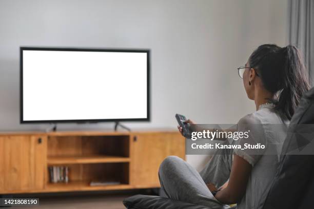 mid adult indonesian woman changing channels with remote control while watching tv - disconnect filme imagens e fotografias de stock