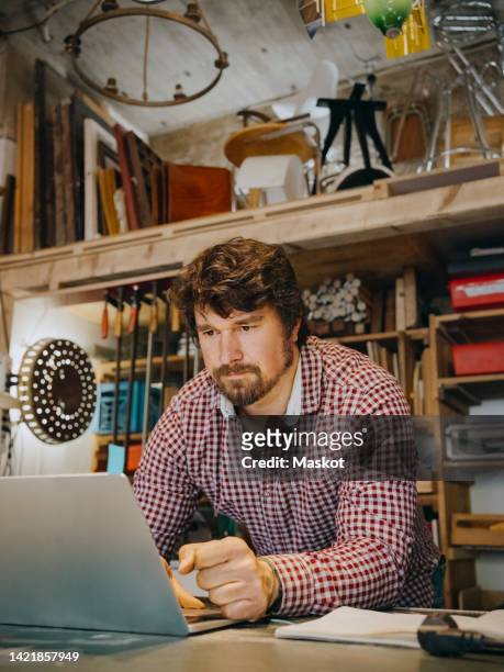 mature craftsman using laptop while working at antique shop - antique shop stock-fotos und bilder