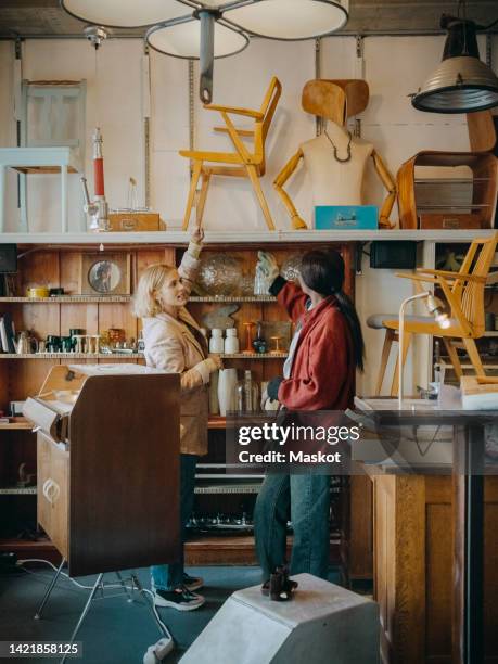 female customer with carpenter pointing at vintage chair on rack in workshop - antiquario foto e immagini stock