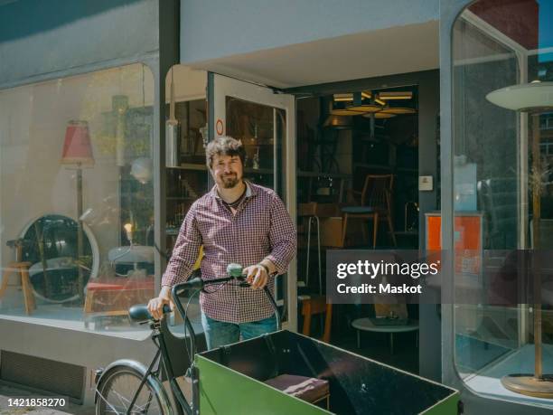 portrait of craftsman with cargo bike standing at entrance of antique store on sunny day - antique shop stockfoto's en -beelden