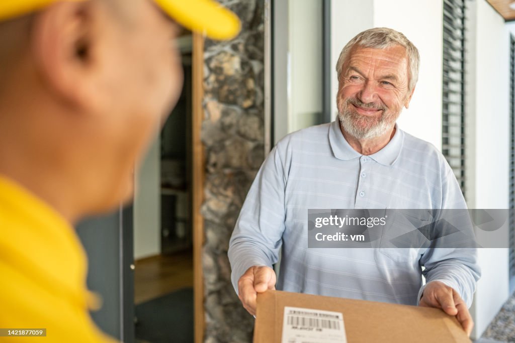 Dokumentenlieferung an die Tür, lächelnder älterer erwachsener Kunde, der Umschlag vom Kurier erhält