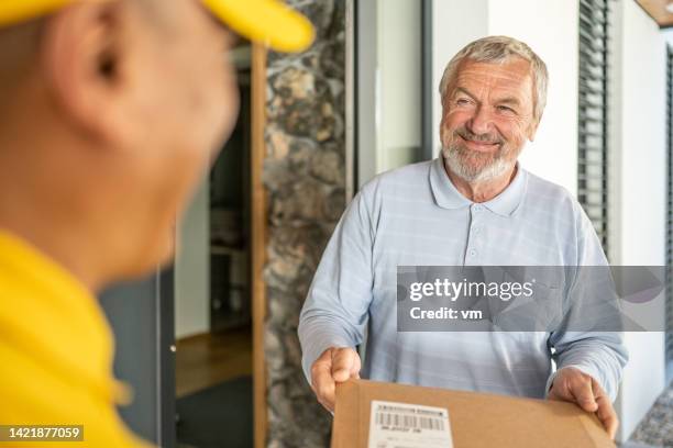 documents delivery to door, smiling senior adult customer getting envelope from courier - postbode stockfoto's en -beelden
