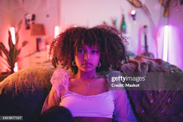 portrait of confident afro woman with curly hair sitting against bed at home - hair curls photos et images de collection