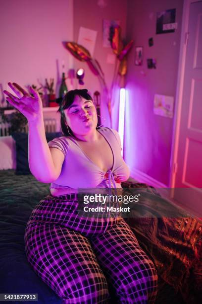 hipster woman with hand raised enjoying in illuminated bedroom at home - fat woman dancing stock pictures, royalty-free photos & images