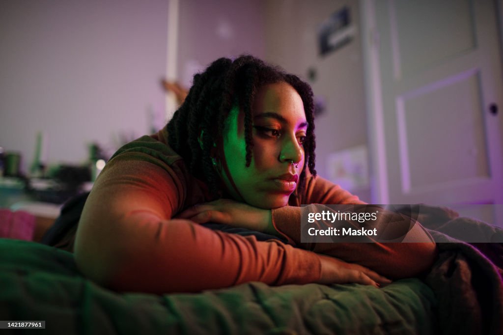 Thoughtful sad non-binary person lying on bed at home