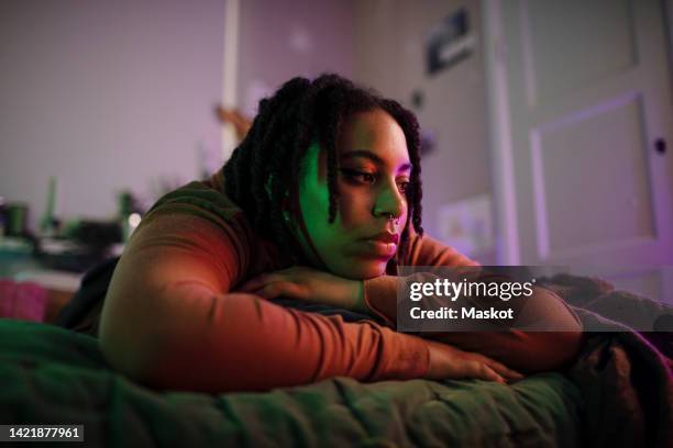 thoughtful sad non-binary person lying on bed at home - depressie stockfoto's en -beelden