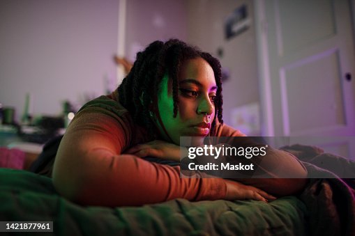 Thoughtful sad non-binary person lying on bed at home Thoughtful sad non-binary person lying on bed at home