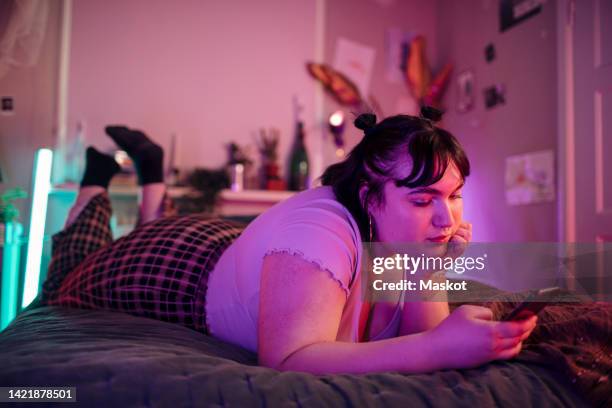 full length of woman with head in hand using mobile phone while lying on bed at home - lichaamsbewustzijn stockfoto's en -beelden