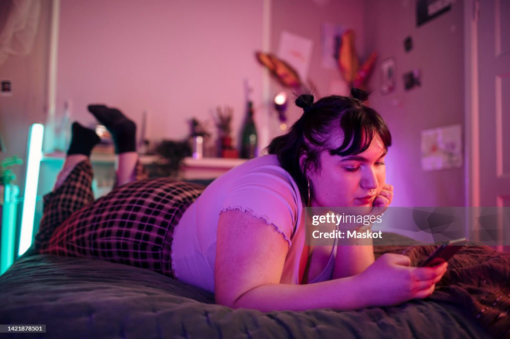 Full length of woman with head in hand using mobile phone while lying on bed at home