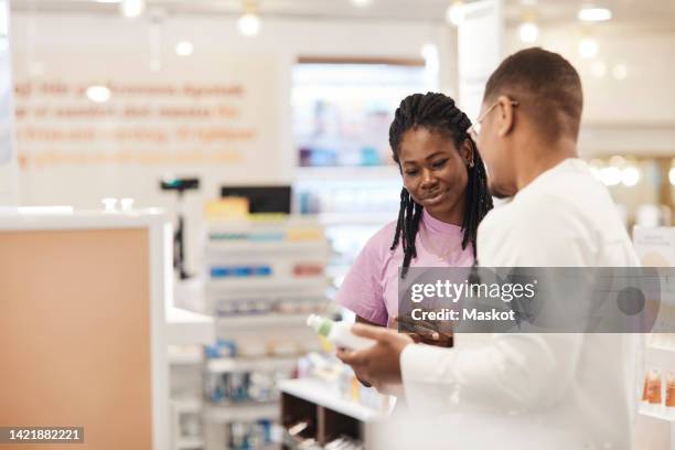 young woman listening to advice of male pharmacist at pharmaceutical industry - pharmacist stock-fotos und bilder