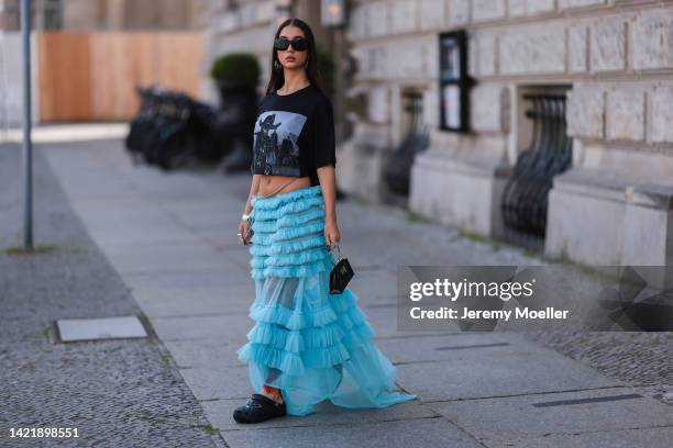 Alina Kossan is seen wearing black Prada sunglasses, silver earrings, black printed cropped oversize Bondy t-shirt, blue transparent tulle ruffled...