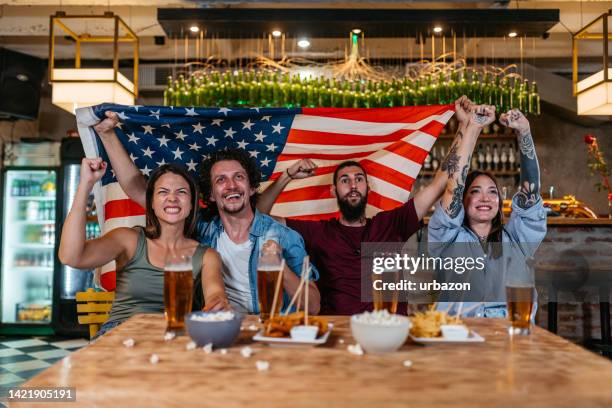 group of friends watching a sports game in a bar and rooting for usa - fútbol americano stock pictures, royalty-free photos & images