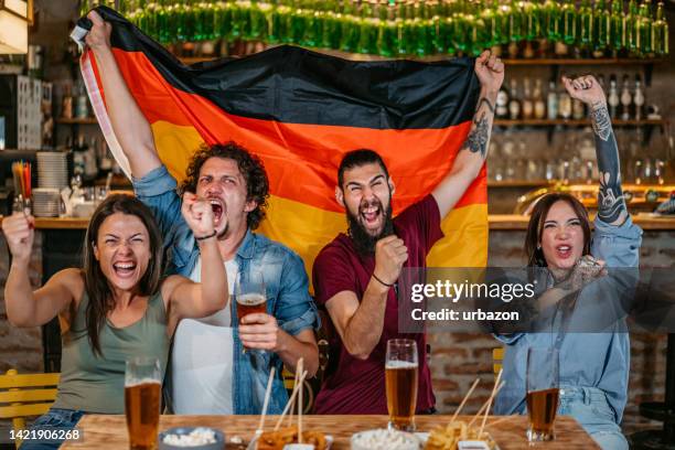 group of friends watching a sports game in a bar and rooting for germany - german culture stockfoto's en -beelden