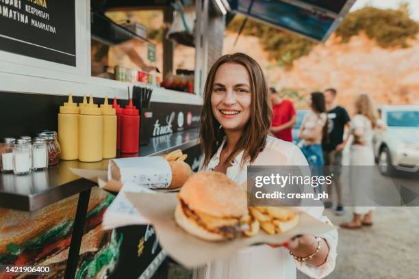 donna sorridente che compra hamburger e patatine fritte al camion di cibo - furgone ambulante foto e immagini stock