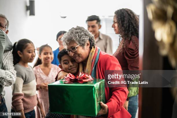 grandmother giving christmas present to grandson while family enters home - prima volta imagens e fotografias de stock