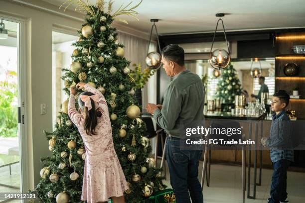 father and daughter decorating the christmas tree in the living room at home - decorating the christmas tree stock pictures, royalty-free photos & images
