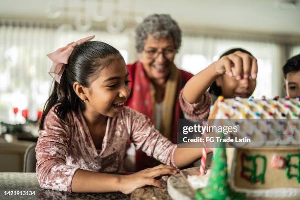 granddaughters making gingerbread house with grandmother at home - gingerbread house stock pictures, royalty-free photos & images