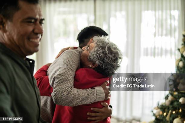 young man embracing grandmother on christmas time at home - visit grandmother stock pictures, royalty-free photos & images