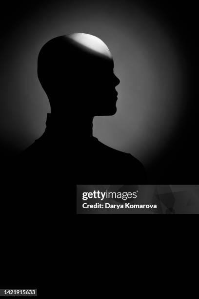 young unrecognizable woman with alopecia in shadow on dark background. a beam of light falls on the problematic bald head of the model, while the face remains in shadow. - female head no hair stock-fotos und bilder