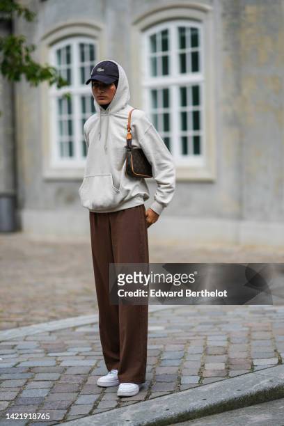 Guest wears a black cap from Lacoste, a beige hoodie sweater, a brown LV monogram print pattern in coated canvas shoulder bag from Louis Vuitton,...