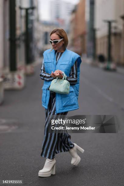 Sonia Lyson is seen wearing silver Bottega Veneta shades, white/blue striped Milk long dress, Remaik blue puffer vest, Zara white platform boots and...