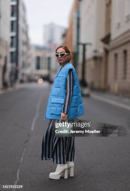 Sonia Lyson is seen wearing silver Bottega Veneta shades, white/blue striped Milk long dress, Remaik blue puffer vest, Zara white platform boots and...