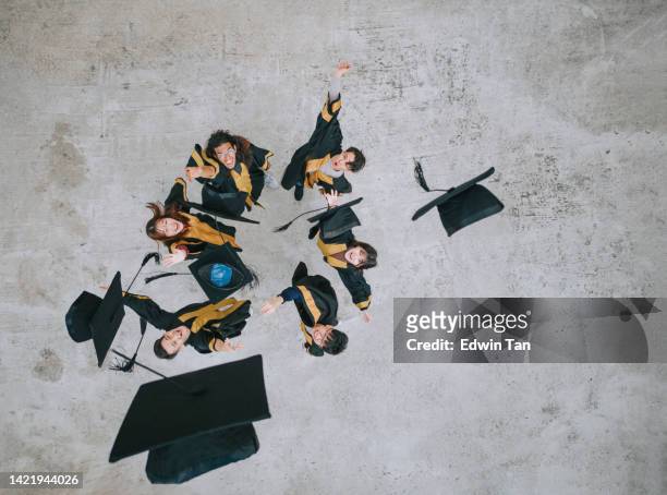 directly below excited asian students tossing mortarboard in the air on graduation day tradition - graduation excitement stock pictures, royalty-free photos & images