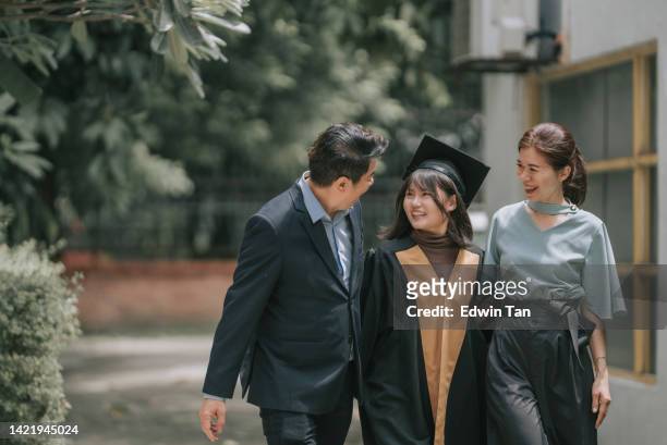 orgullosos padres chinos caminando junto con su hija con batas de graduación en la universidad - university students celebrate their graduation fotografías e imágenes de stock