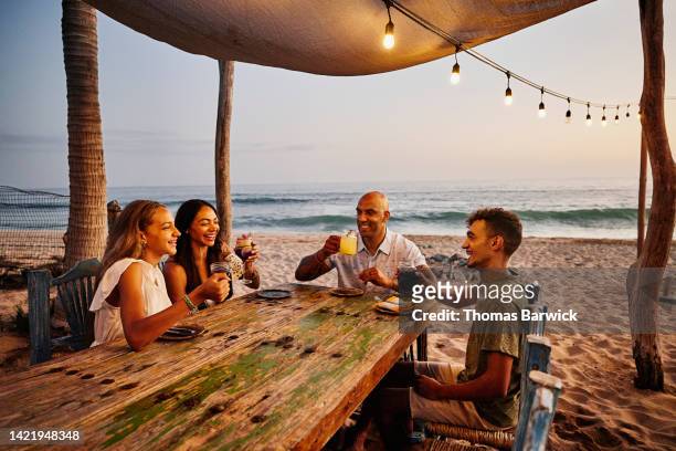 wide shot of smiling family enjoying drinks at tropical beach restaurant - familie hell weiss stock-fotos und bilder