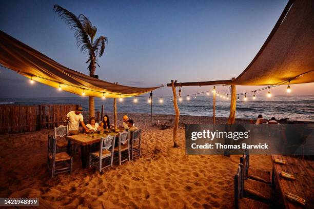 wide shot of waiter serving family food at tropical beach restaurant - couple sand sunset stock pictures, royalty-free photos & images
