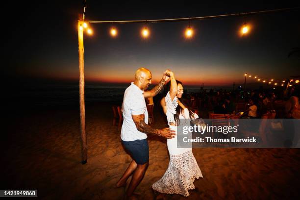 wide shot of smiling couple dancing under lights at beach restaurant - tropical beach holiday stock pictures, royalty-free photos & images