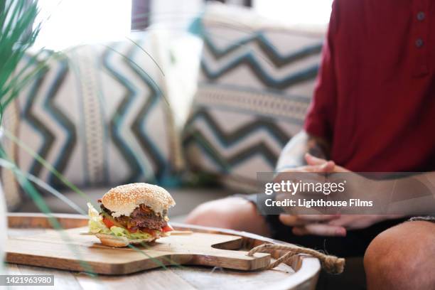 male sits in front of half eaten savory cheeseburger on cutting board - bacon cheeseburger stock-fotos und bilder