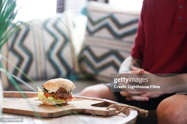 male sits in front of half eaten savory cheeseburger on cutting board - bacon cheeseburger stockfoto's en -beelden