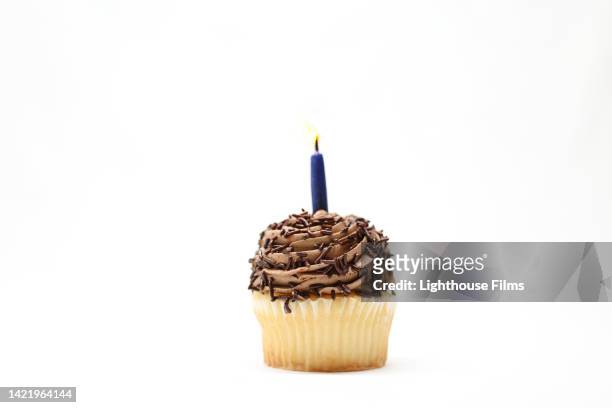 tasty vanilla cupcake with chocolate frosting and lit birthday candle - birthday cake white background stock pictures, royalty-free photos & images