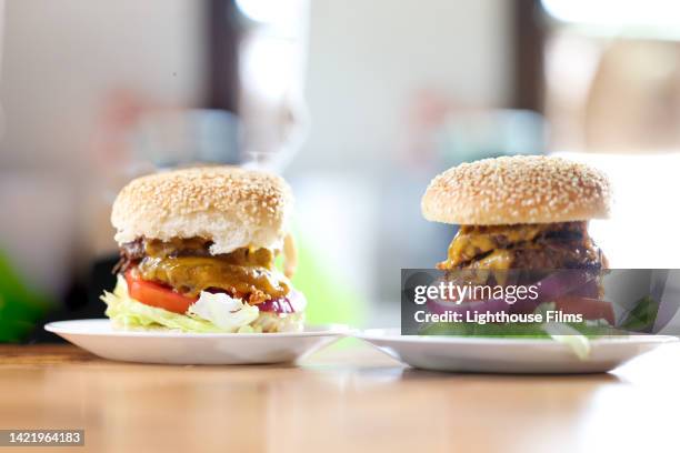 two savory cheeseburgers with fresh ingredients on a wood table - sesame seed bun stock pictures, royalty-free photos & images