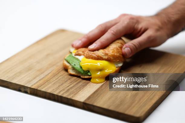 hand presses crossiant breakfast sandwich and egg yolk runs out - arm made of vegetables stock pictures, royalty-free photos & images