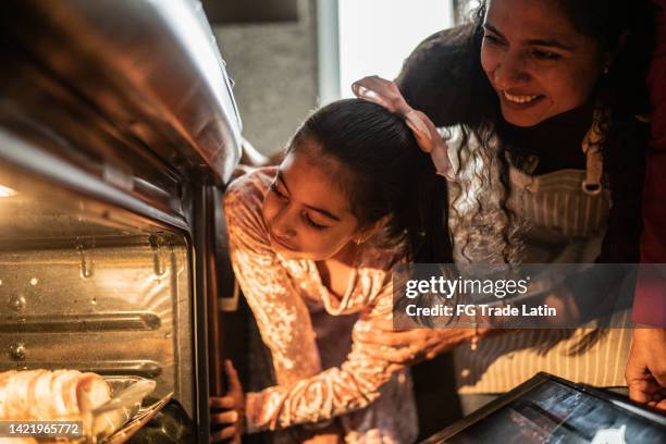 mother and daughter looking at food in the oven at home - mother daughter cooking stock pictures, royalty-free photos & images