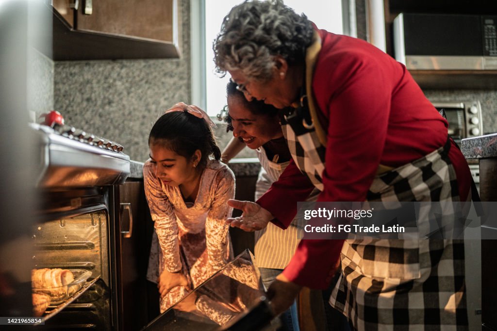 Grandmother, mother and daughter looking at food in the oven at home
