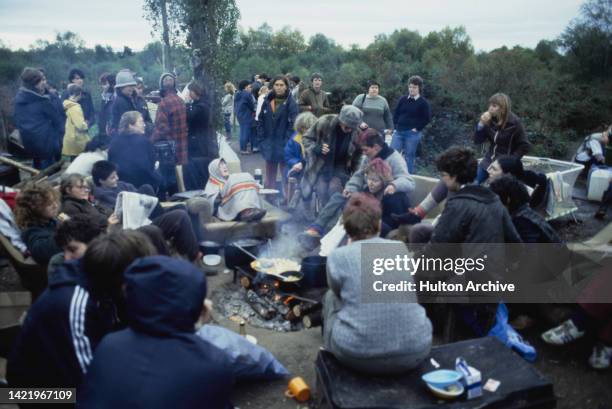 Women at the Greenham Common Women's Peace Camp around a camp fire at RAF Greenham Common, Berkshire, UK, circa 1983. The camp was set up by women...