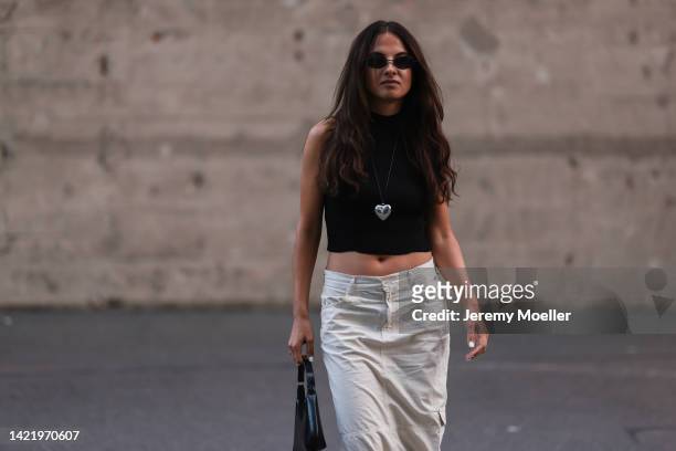 Anna Winter is seen wearing black shades, black sleeveless top, heart shape pendant necklace and beige cargo midi skirt, black shiny leather bag,...