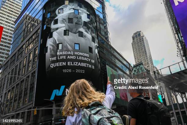 People point to a the Nasdaq billboard displaying a message honoring the life and legacy of Queen Elizabeth II in Times Square on September 08, 2022...