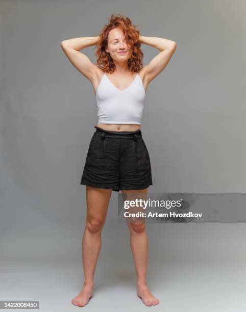positive face emotion  of red head , curly haired woman dressed in white tank top. - barefoot redhead ストックフォトと画像